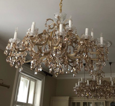 Grand chandelier with crystal accents hanging in a room with a window and furniture.
