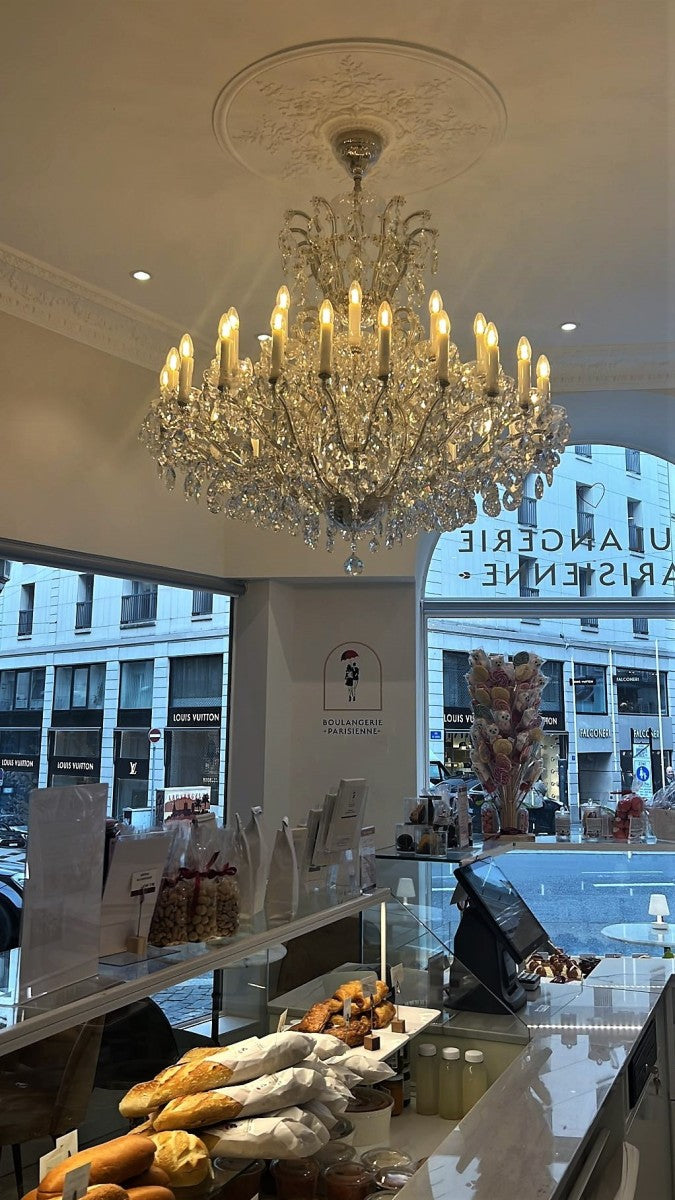 Crystal chandelier hanging in a store with a display of bread and a cityscape outside.