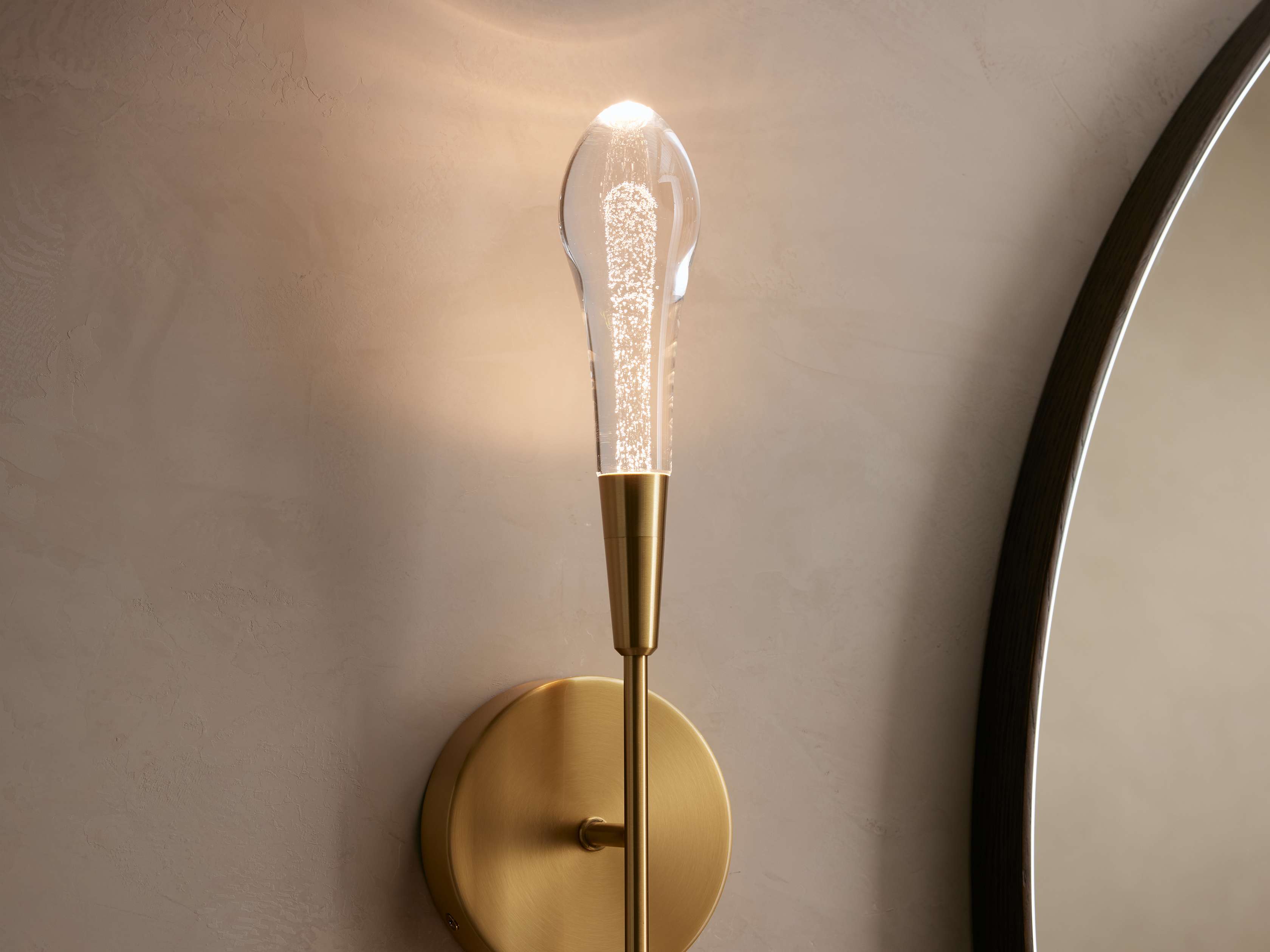 Gold wall sconce with a clear light bulb on a neutral wall.